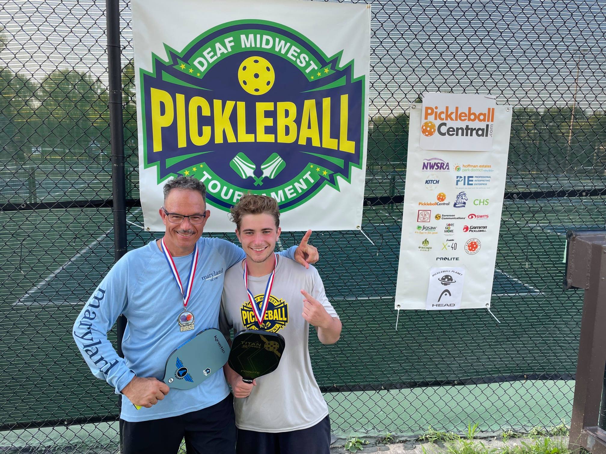 Kevin Hall and Sean Trapp standing in front of Deaf Midwest Pickleball logo. Both holding a paddle with medals around their necks