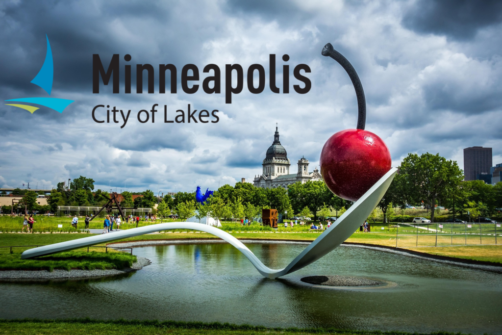 Sculpture of a spoon with cherry on it on a small pond. City of Minneapolis in the background. Text: "Minneapolis: City of Lakes"